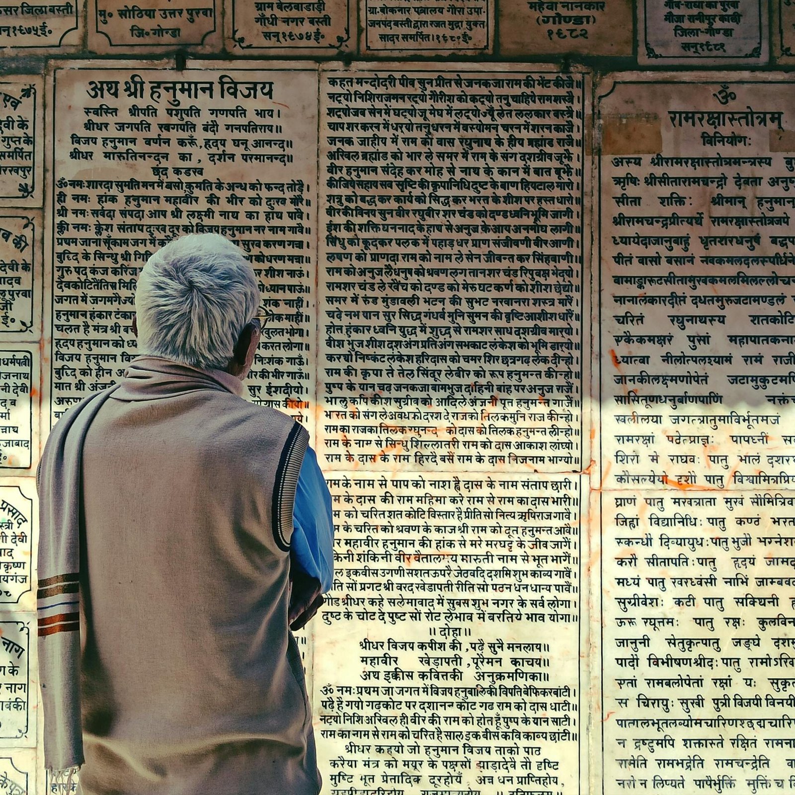 Elderly man reads ancient scriptures on temple wall in Bodh Gaya, India, rich in cultural heritage.