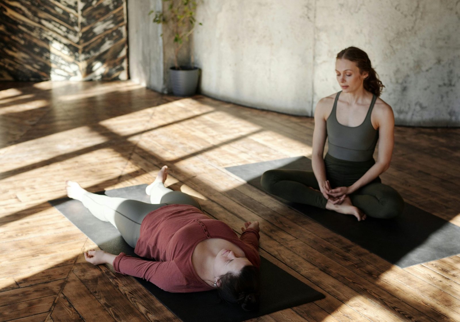 Two women practicing yoga indoors with sunlight streaming in, highlighting focus and relaxation.