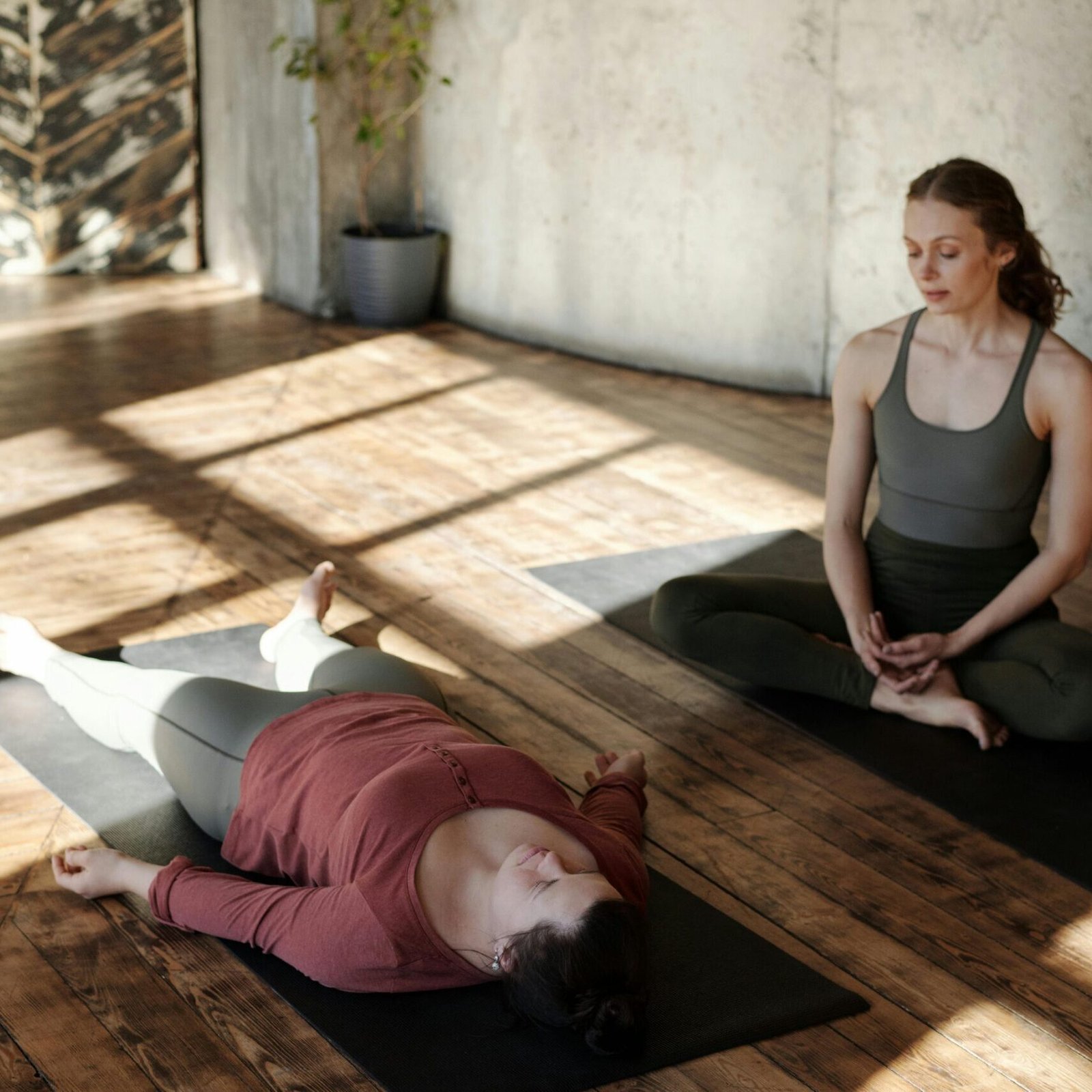 Two women practicing yoga indoors with sunlight streaming in, highlighting focus and relaxation.